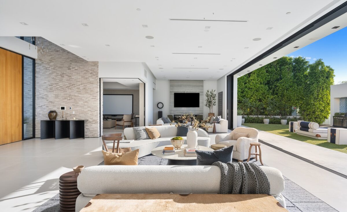 Un salon blanc spacieux dans une maison luxueuse relié à un grand patio extérieur